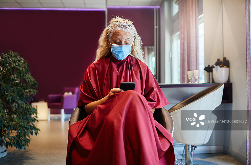 疫情期间戴着口罩在美发沙龙使用智能手机的女人图片素材