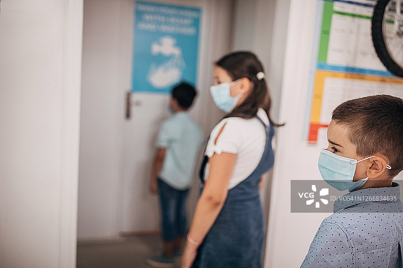 戴口罩的孩子们排队等待使用卫生间，保持安全距离图片素材