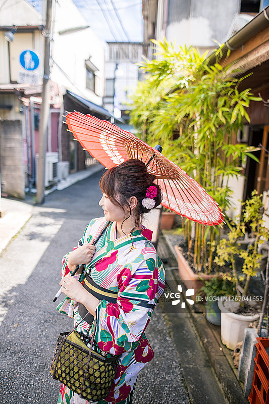 身穿浴衣的年轻女人走在日本老街上，拿着红色纸伞图片素材