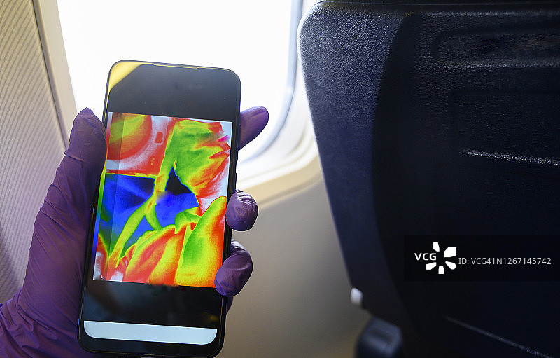手持智能手机，显示飞机舷窗附近的热成像图片素材