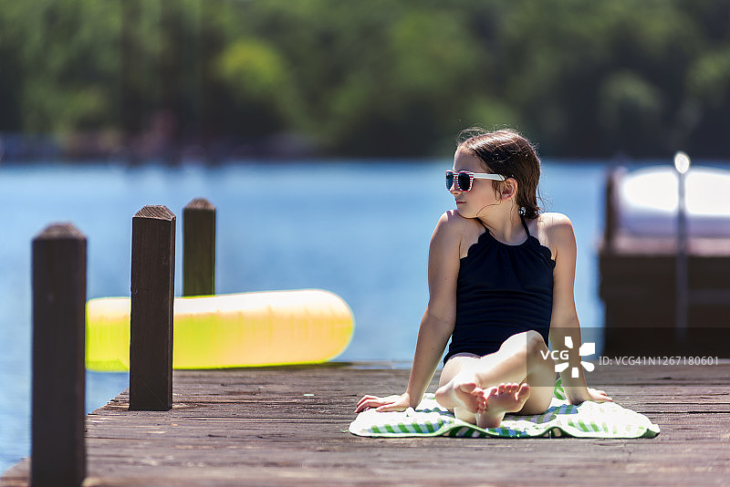 年轻女孩穿着泳衣坐在湖边码头的沙滩巾上图片素材