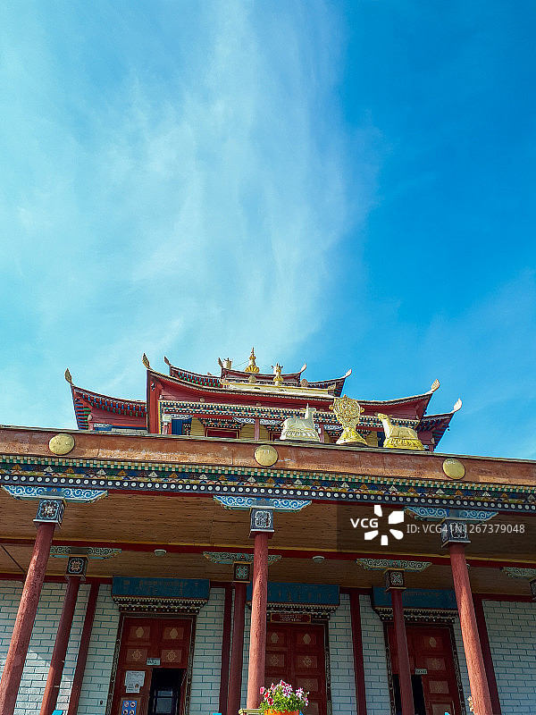美丽的佛教寺院，拥有色彩缤纷的木雕、象征性装饰、花卉云朵以及夏季明亮蓝天下金色小鹿动物雕像图片素材