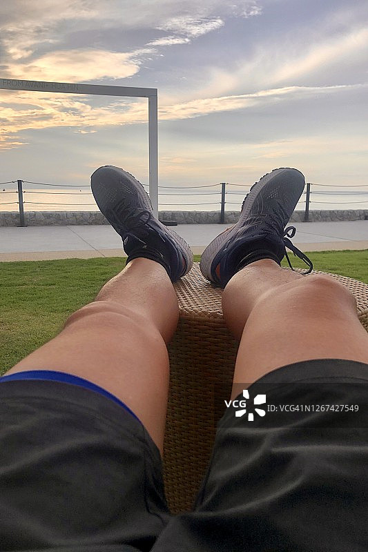 华欣海边的清晨天空，一位男士在沙滩椅上放松腿部图片素材