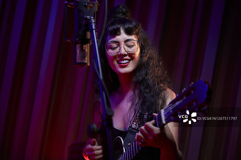 混血女音乐家在录音棚里唱歌、弹吉他并录制人声图片素材