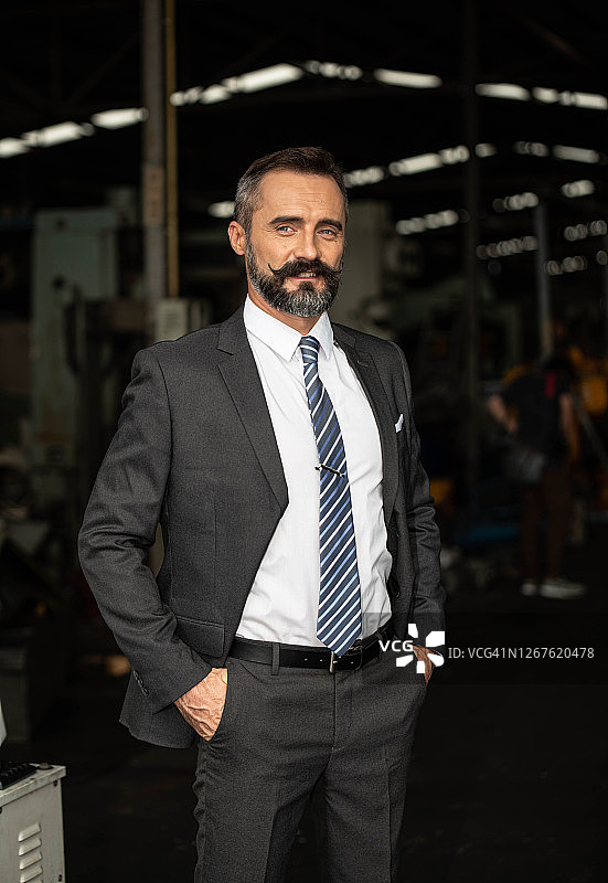 身穿漂亮西装、头戴头盔的迷人胡须工厂经理在工业工厂内图片素材