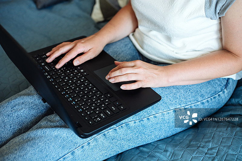 在床上用笔记本电脑在家工作的女人，手和键盘特写，居家、在家工作、远程工作区和家庭办公室的概念图片素材