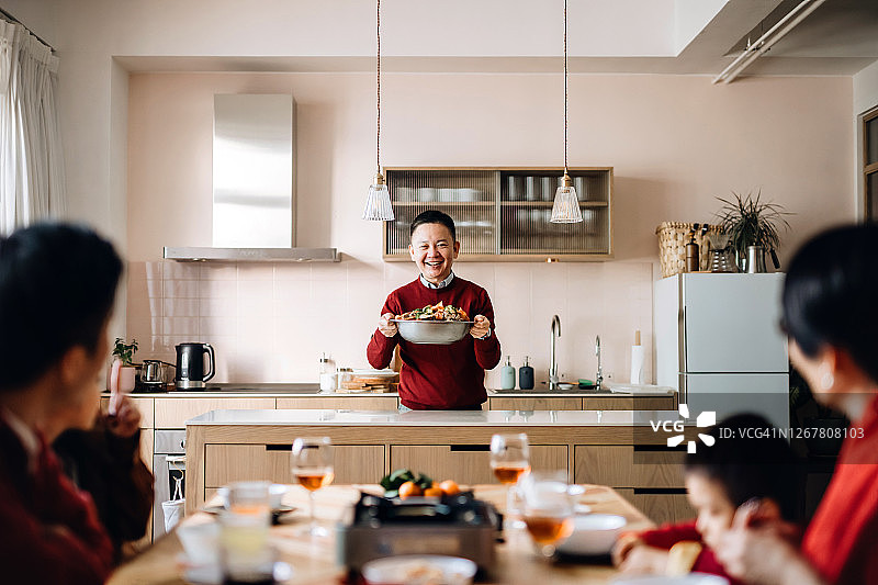 三代亚洲家庭欢庆中国新年，祖父在团圆饭上供应美味的传统中国盆菜图片素材