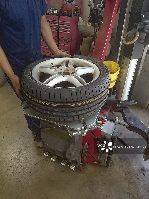 在车库里，修理工在轮胎更换机的帮助下，将轮胎安装在轮辋上图片素材