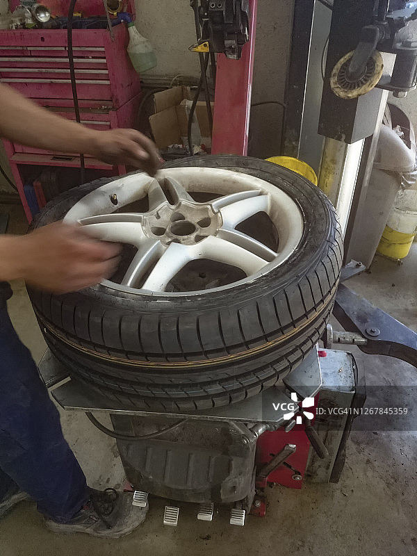 在车库里，修理工在轮胎更换机的帮助下，将轮胎安装在轮辋上图片素材