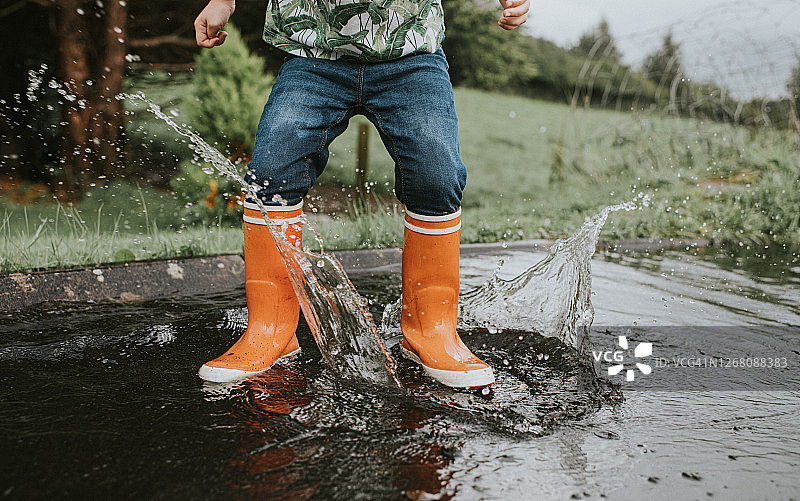 穿着橙色雨靴在深水坑中跳跃的儿童图片素材