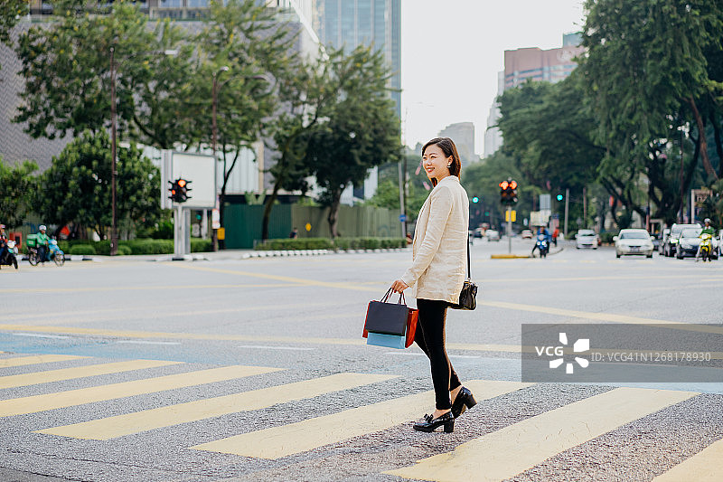 亚洲女商人提着购物袋过马路图片素材