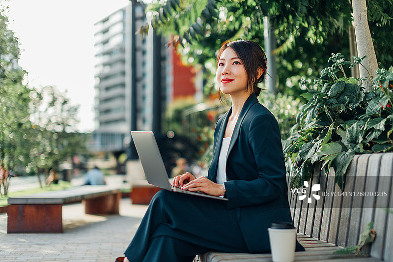 在公园长椅上使用笔记本电脑的年轻女商人图片素材