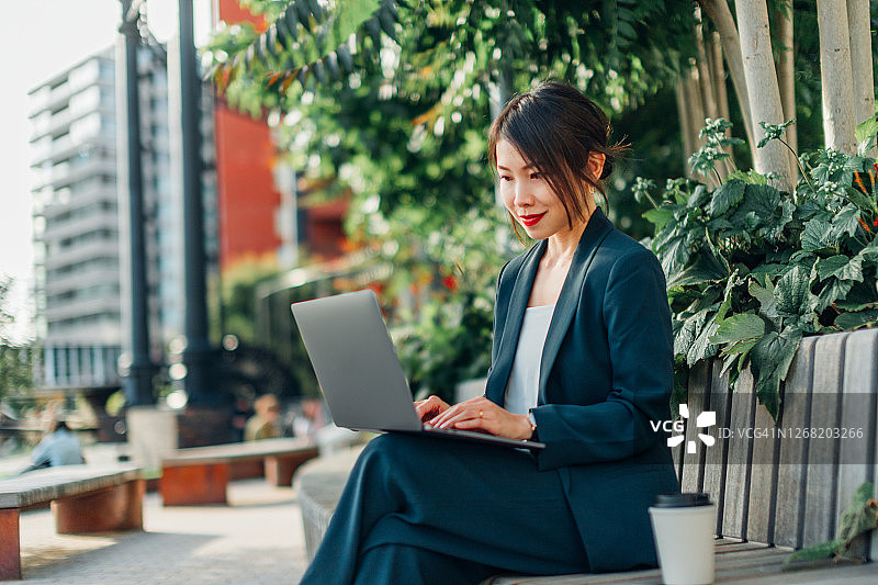 在公园长椅上使用笔记本电脑的年轻女商人图片素材