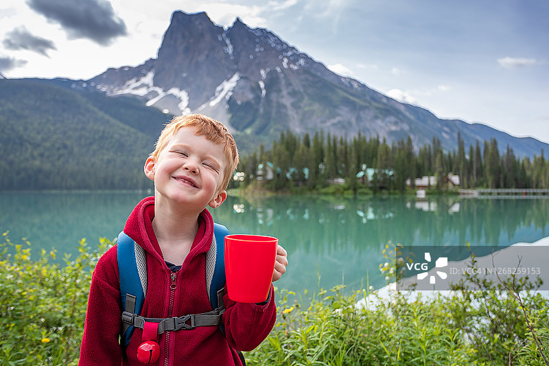 在夏天绿宝石湖边微笑的快乐的年轻可爱红发男孩图片素材