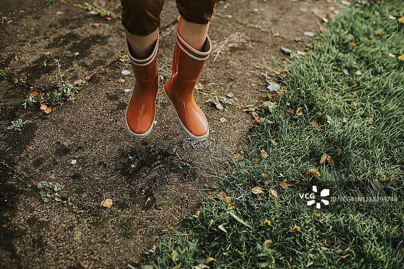 孩子穿着亮橙色的雨靴跳跃图片素材