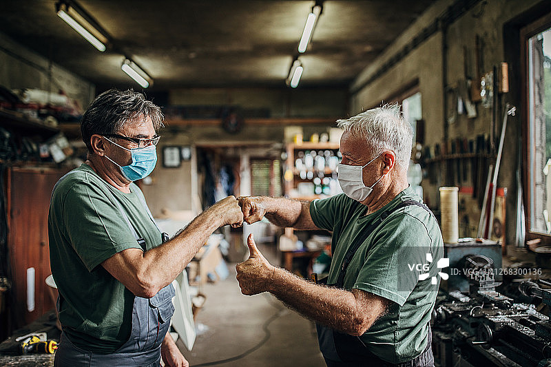 在车间里戴着防护口罩碰拳的同事图片素材