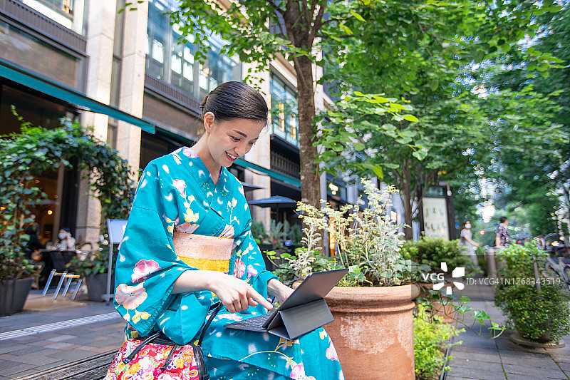 身穿浴衣坐在长椅上使用平板电脑的年轻女子图片素材