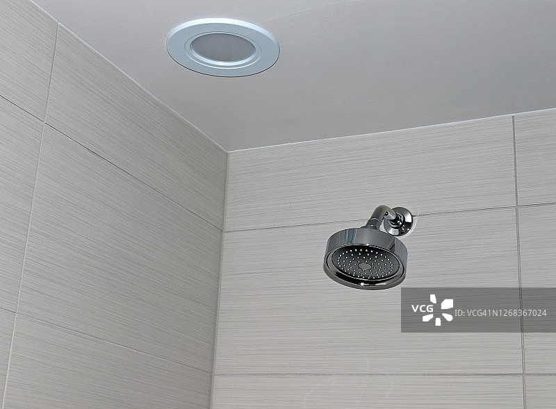 浴室瓷砖墙上的淋浴喷头和天花板上的圆形灯具图片素材
