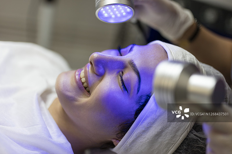 女美容师为年轻女子面部进行蓝光护理图片素材