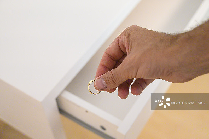 男人戴着金色结婚戒指，仔细观察后将其放入白色抽屉图片素材