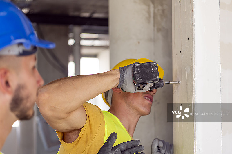 男人手里拿着一个红色钻头，装修的概念，自制的手工。悬挂架子，整理带照片的相框，公寓装修。图片素材