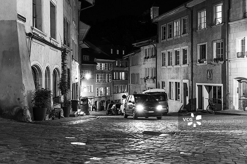 瑞士弗里堡老城夜晚的鹅卵石街道上的汽车图片素材