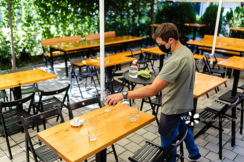 服务员在顾客离开后收拾空杯子，同时拿着装有消毒液和抹布的托盘图片素材