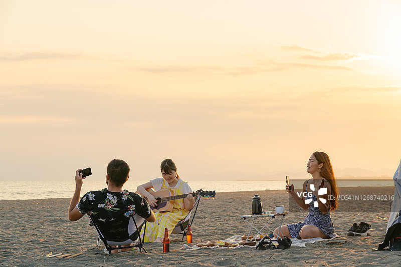 一群朋友在海滩日落时享受音乐、饮料和烧烤图片素材