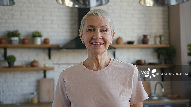 穿着粉色T恤，面带微笑，看向镜头的快乐老妇人图片素材