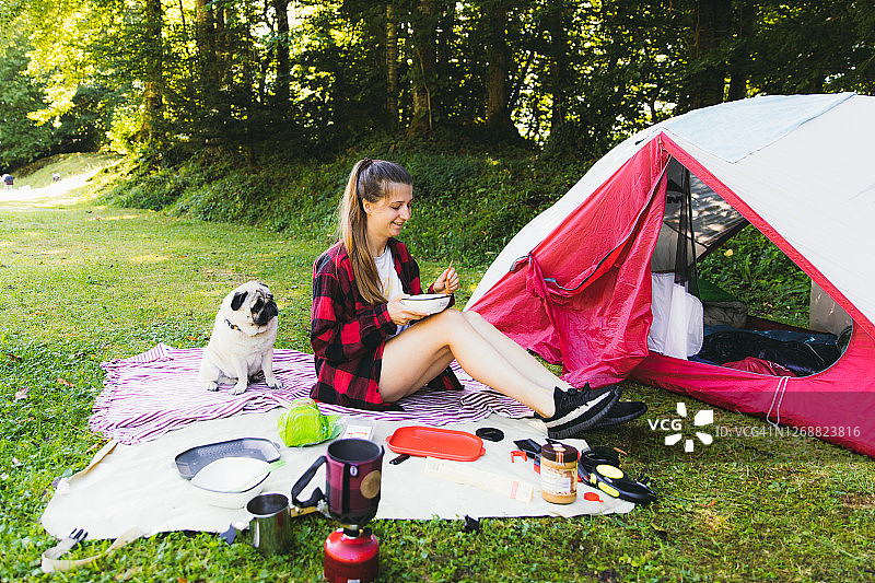 年轻女游客在瑞士的露营地帐篷附近与她的狗一起享用早餐图片素材