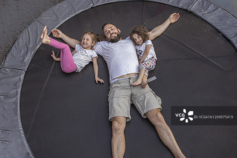 爸爸和女儿在蹦床上跳跃后休息图片素材