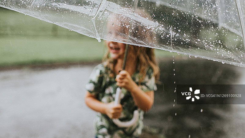 快乐的小女孩在暴风雨中拿着雨伞——聚焦雨伞和雨滴图片素材