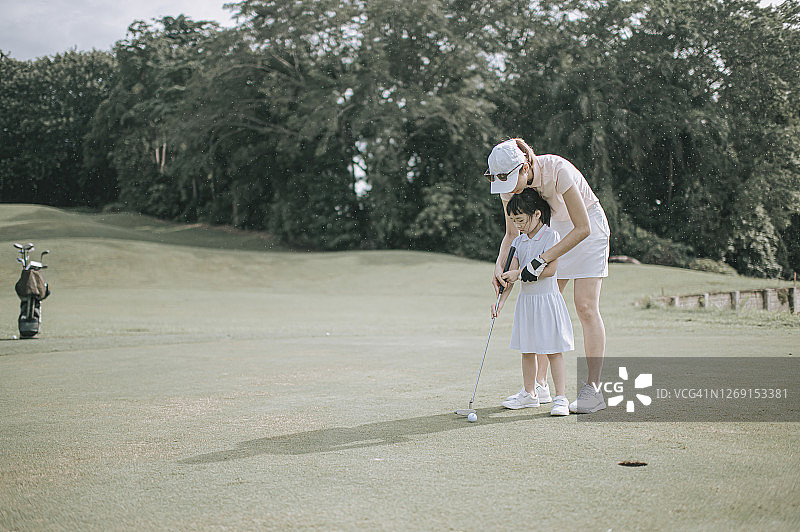 亚洲中国父母高尔夫球手教女儿在高尔夫球场周末打高尔夫球图片素材