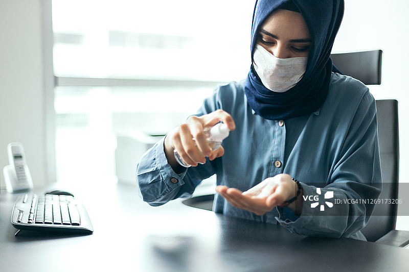 戴头巾的年轻女商人用洗手液消毒双手图片素材