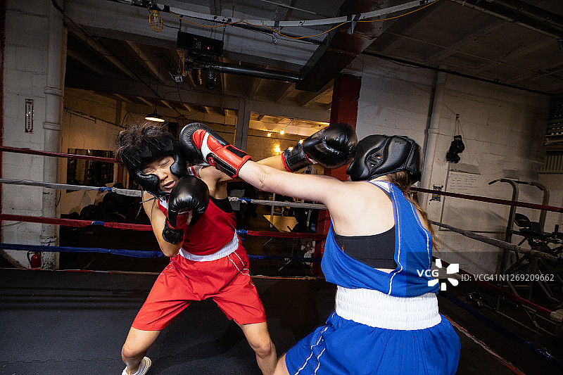 女拳击手与拳击手进行对抗训练，一名拳击手用左手击打头部图片素材