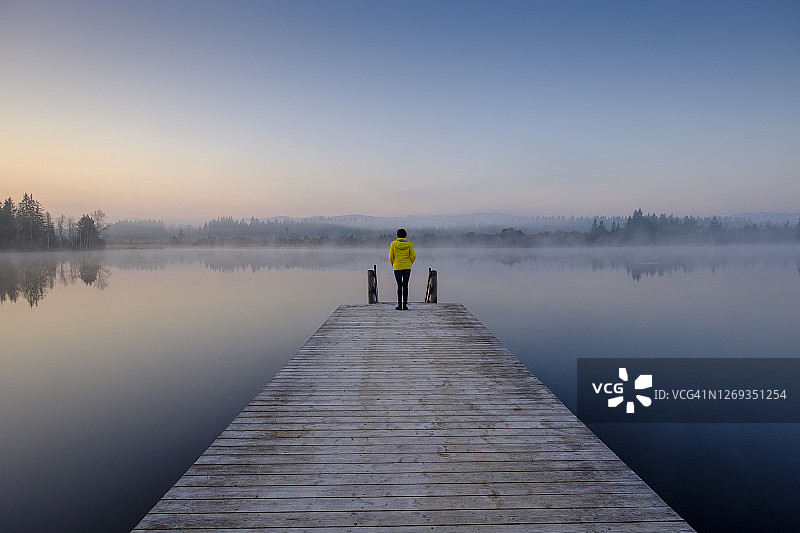 薄雾黎明时分，女子站在湖岸码头边图片素材