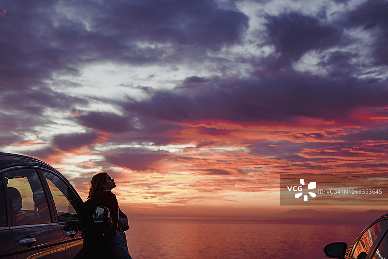 中年女人站在海滩汽车旁，背景是多云的日落图片素材