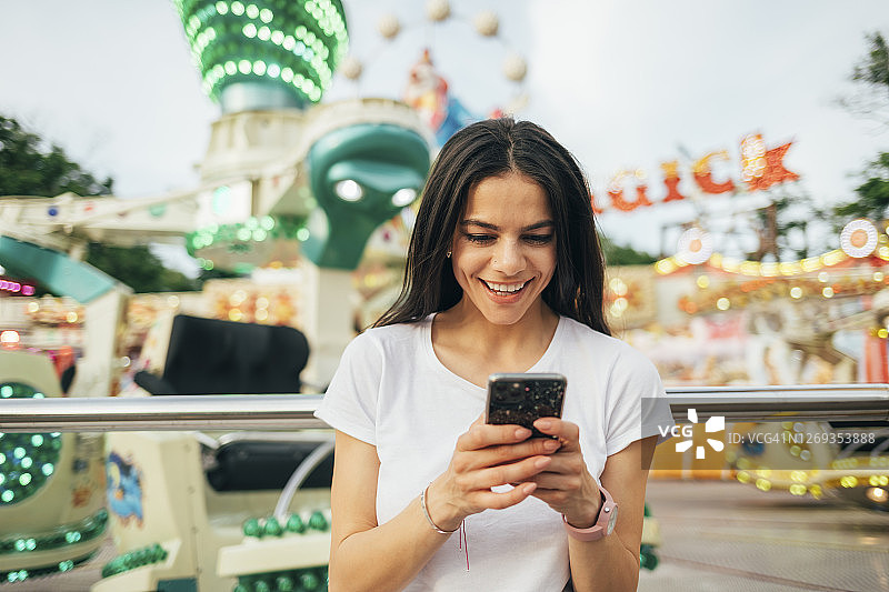 笑容满面的年轻女人站在游乐园里使用智能手机图片素材