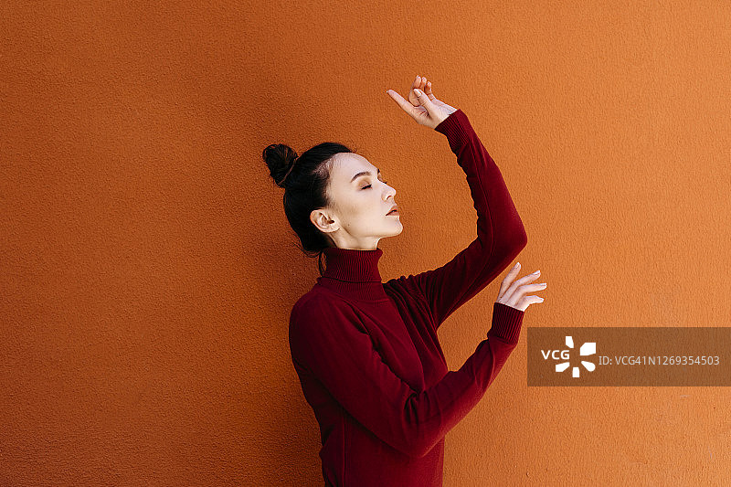 闭着眼睛在橙色墙壁前跳舞的女人图片素材
