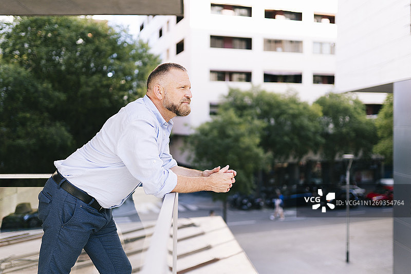 倚靠办公室阳台栏杆沉思的商人图片素材