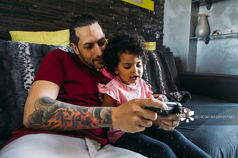 父亲和女儿在家放松地在沙发上玩电子游戏图片素材