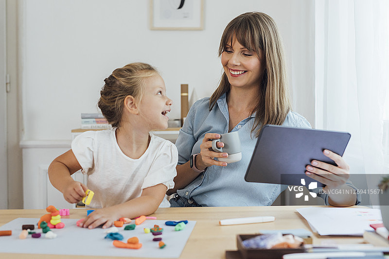 亲子手工：母亲和女儿在家用橡皮泥制作雕像，母亲在家使用数位板工作图片素材