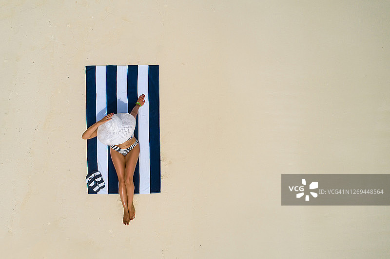 夏季假日时尚概念：在马尔代夫白色沙滩上戴太阳帽的女孩航拍，无人机俯视视角，海滩上享受日光浴的苗条女人图片素材