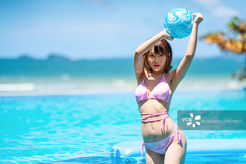 年轻的亚洲女性穿着比基尼，在海边游泳池边拿着沙滩球图片素材