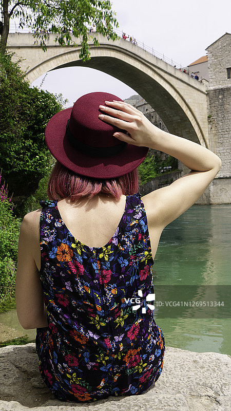 女游客坐在内雷特瓦河岸边，望着古老的桥梁图片素材