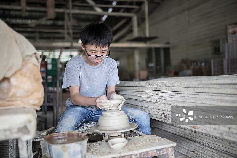 中国少年在拉坯机上制作陶碗，高兴地展示他的作品图片素材