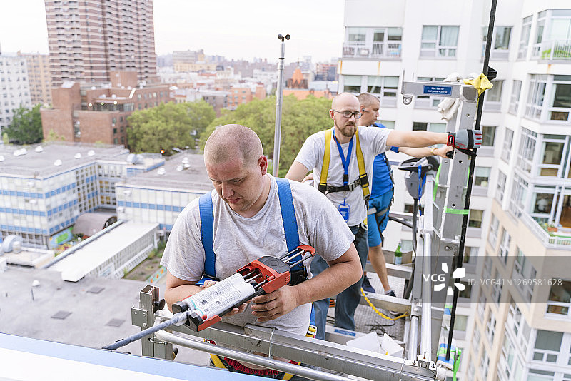 蓝领工人在办公楼更换破损窗户，使用升降平台进行高空作业并涂抹密封胶图片素材