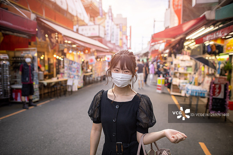 日落时分，戴着口罩在购物街上行走的年轻女人图片素材