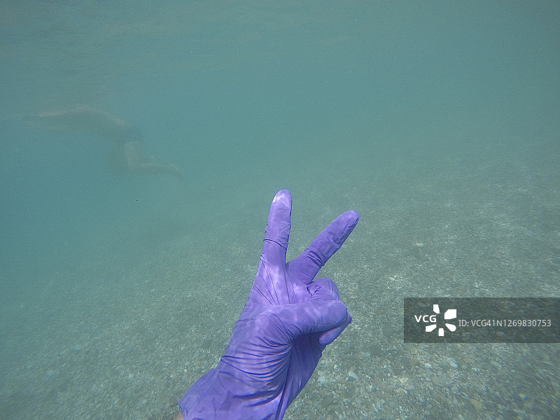 男人戴着手套在西班牙阿尔梅里亚海中潜水，做出胜利手势图片素材
