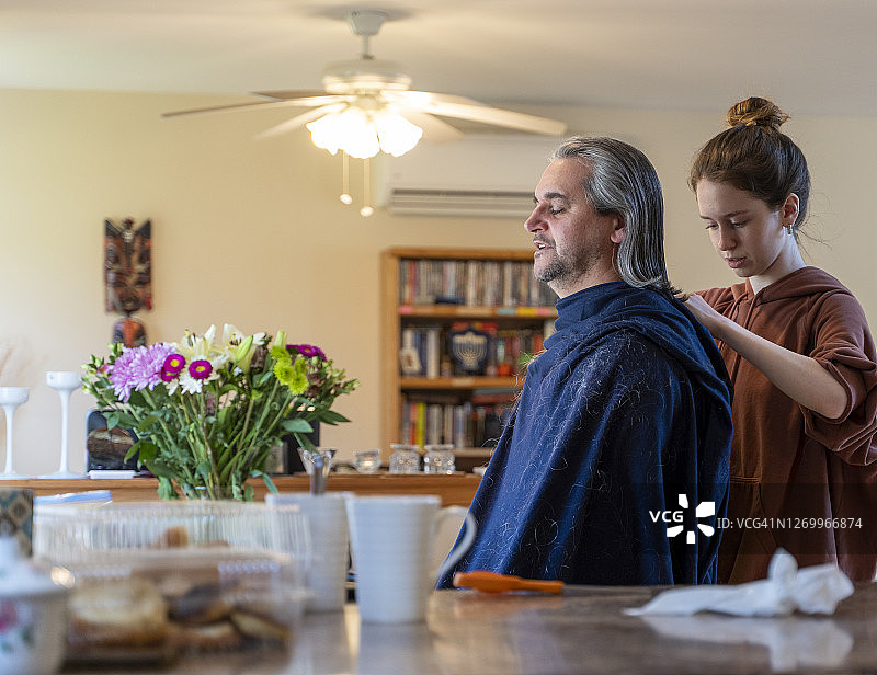 自己动手 - 家庭理发。一个十几岁的女儿给她的父亲，一个50岁留长发的中年男人理发。图片素材